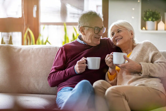 Smiling senior couple enjoying coffee together on the couch, illustrating the comfort and health benefits of mushroom coffee for older adults.